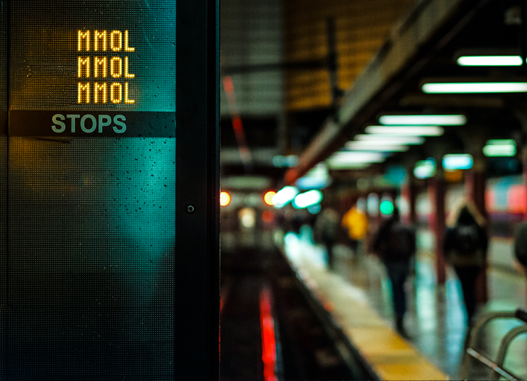 A subway platform sign repeating MMOL in bright lights.